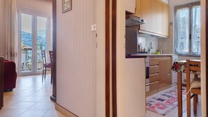 Een keuken met houten kastjes, een eethoek met een rode bank, en uitzicht door de schuifdeuren.