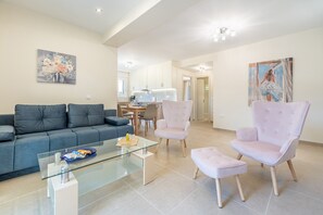 Uma sala de estar moderna com sofá, poltronas, mesa de centro de vidro e um espaço de jantar com mesa e cadeiras.
