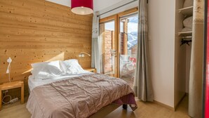 A bedroom with a wooden headboard, a bed with white bedding, a red pendant light, and a view of a balcony with a wooden railing.