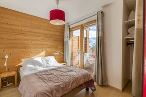 A bedroom with a wooden headboard, a bed with white bedding, a red pendant light, and a view of a balcony with a wooden railing.