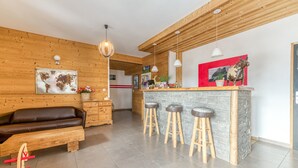 A modern kitchen with a wooden bar area, stools, and a seating area with a sofa and a wooden table.