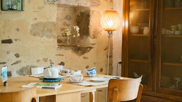 Une table en bois, sur laquelle se trouvent une théière, des tasses et une lampe, dans une pièce rustique aux murs de pierre et agrémentée d’un meuble en bois.