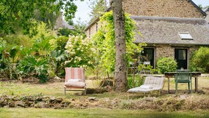 Une maison en pierre avec un jardin, un espace extérieur aménagé pour s’asseoir et un arbre.