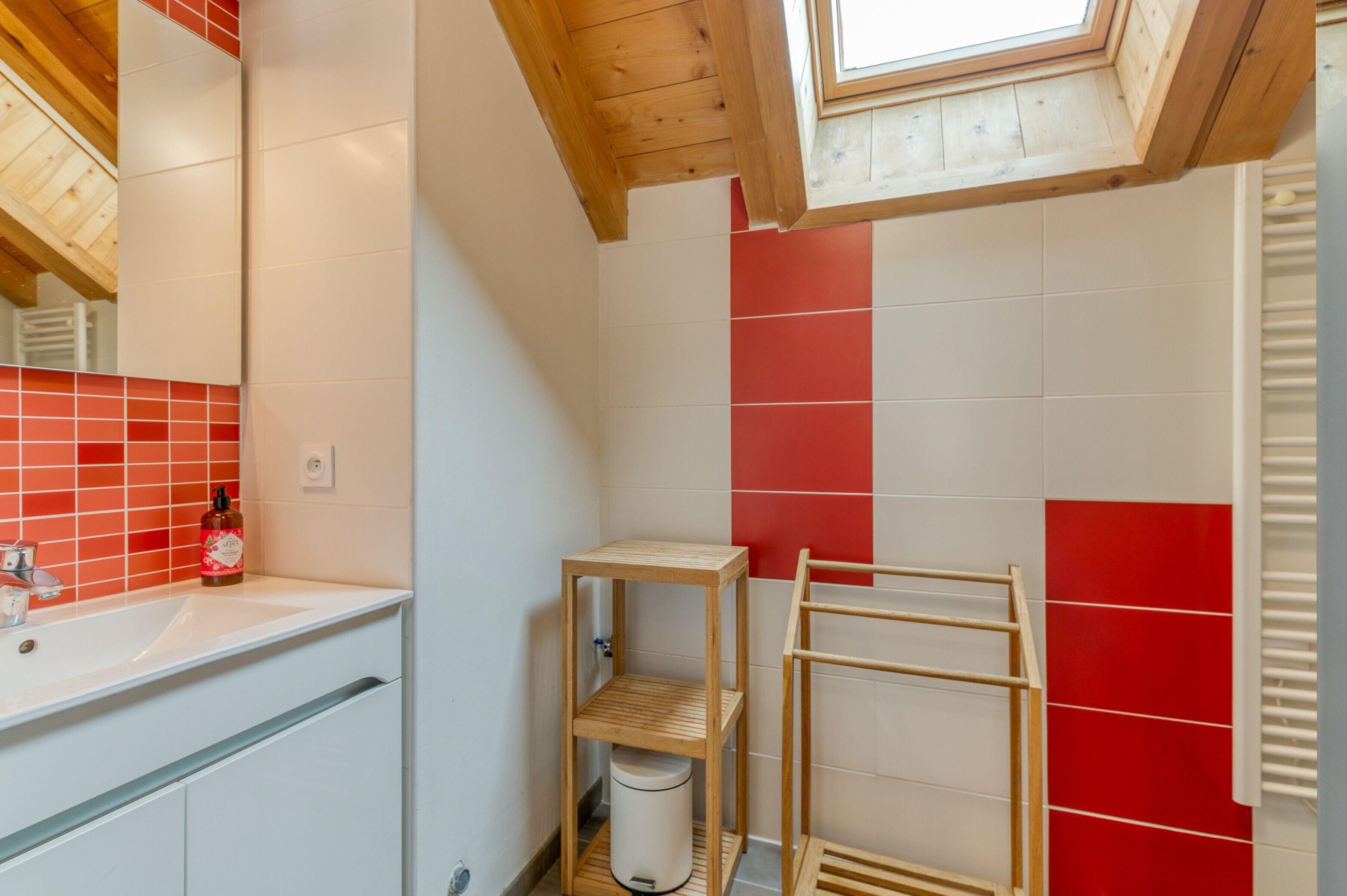 Une salle de bain avec un puits de lumière, un lavabo blanc, un mur recouvert de carreaux rouges et une étagère en bois.