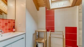 Une salle de bain avec un puits de lumière, un lavabo blanc, un mur recouvert de carreaux rouges et une étagère en bois.
