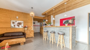 A modern kitchen with a wooden bar area, stools, and a seating area with a sofa and a wooden table.
