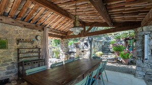 A rustic outdoor dining area with a wooden table and chairs, stone walls, and potted plants. - Villa 'L'Elzède' with Mountain Views, Private Pool and Wi-Fi (Les Vans)