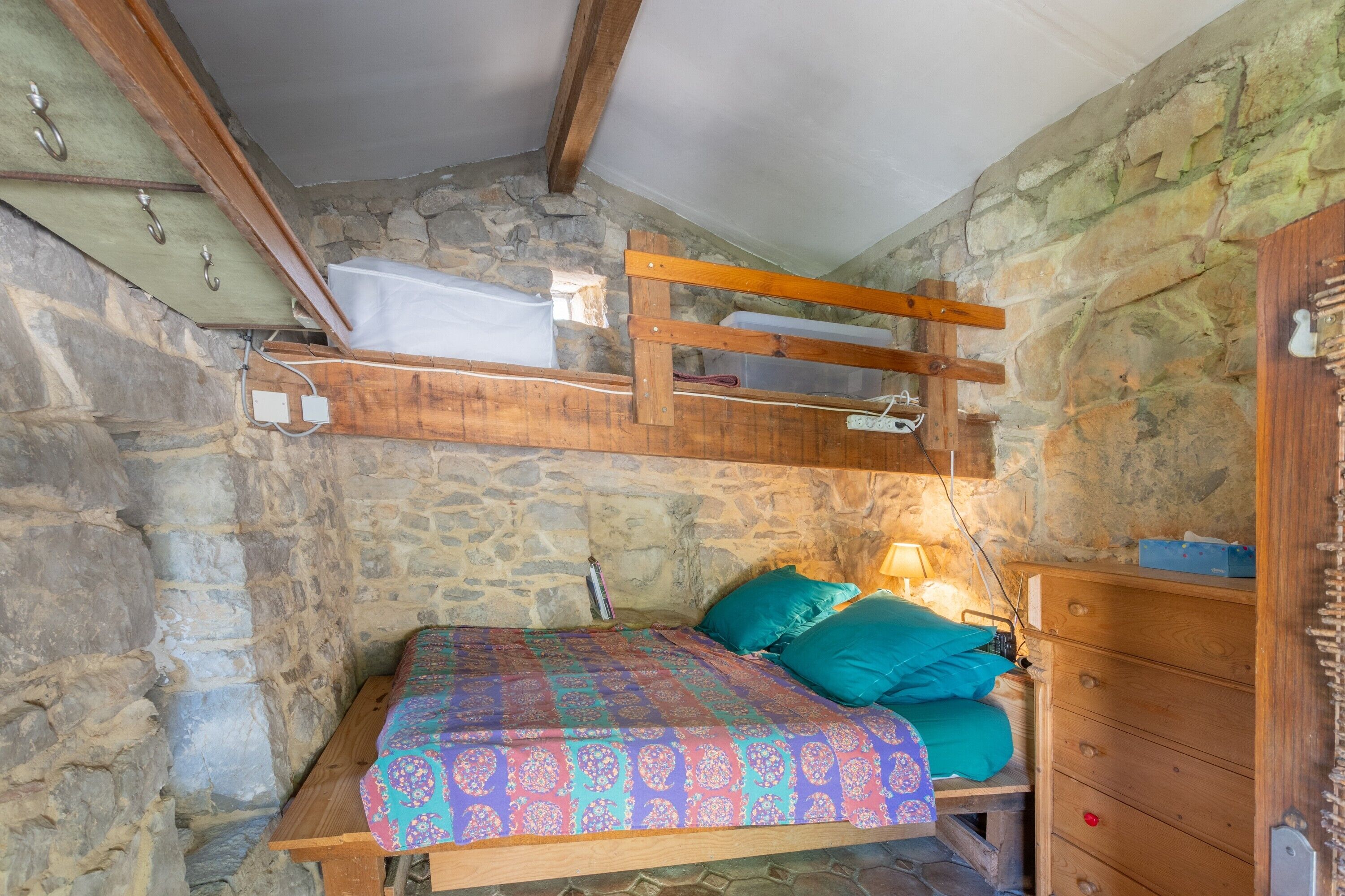 A stone-walled room with a bed, wooden furniture, and a slanted ceiling.