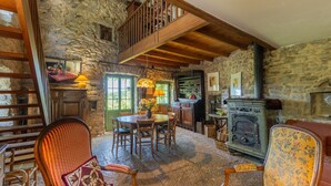A rustic interior with a stone wall, wooden beams, a dining area with chairs, a table, and a fireplace. - Villa 'L'Elzède' with Mountain Views, Private Pool and Wi-Fi (Les Vans)
