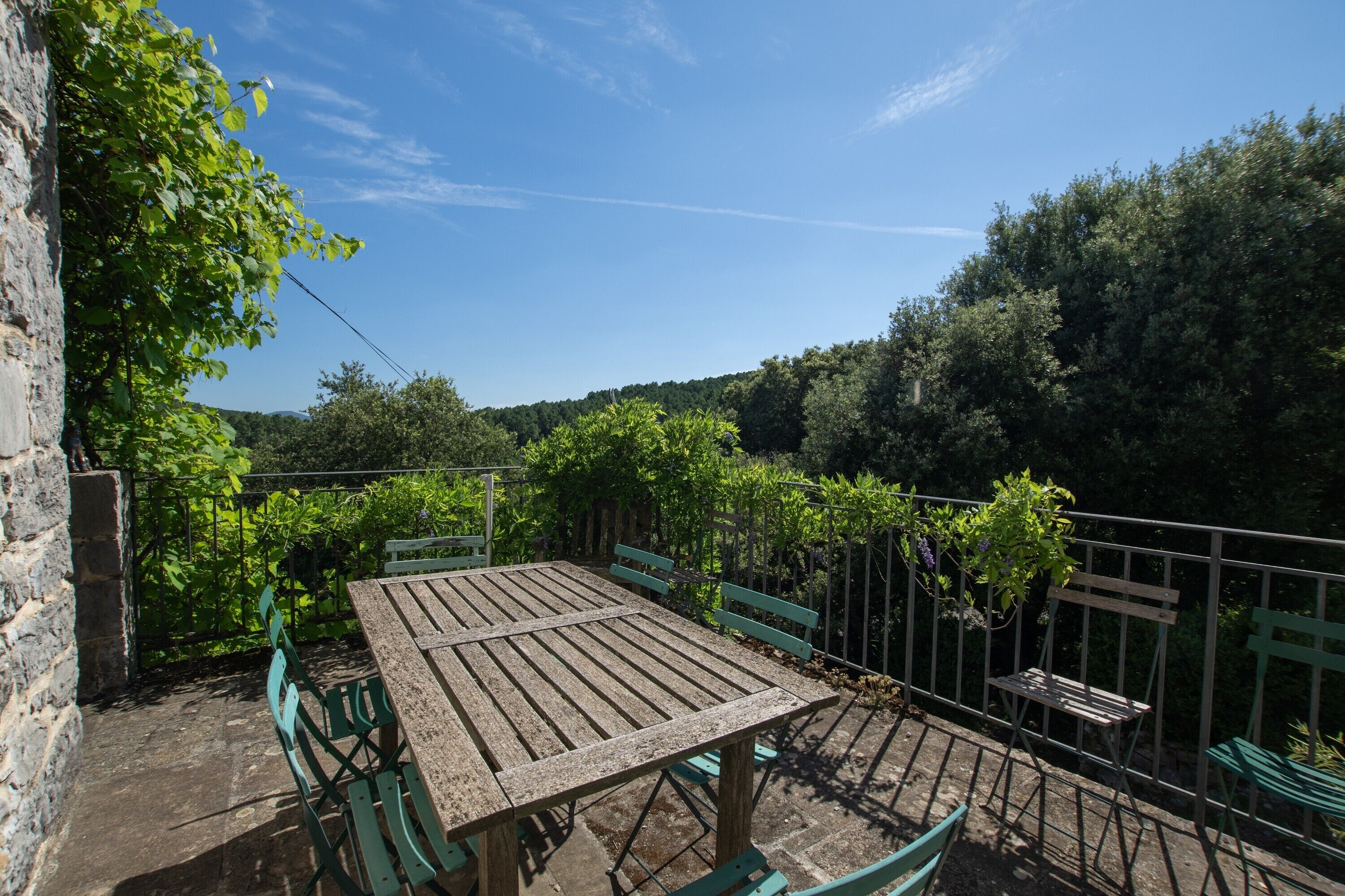 A wooden table with chairs, a stone wall, and a metal fence in a garden setting.
