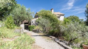 A stone building with a tiled roof, surrounded by olive trees and a gravel path. - Villa 'L'Elzède' with Mountain Views, Private Pool and Wi-Fi (Les Vans)