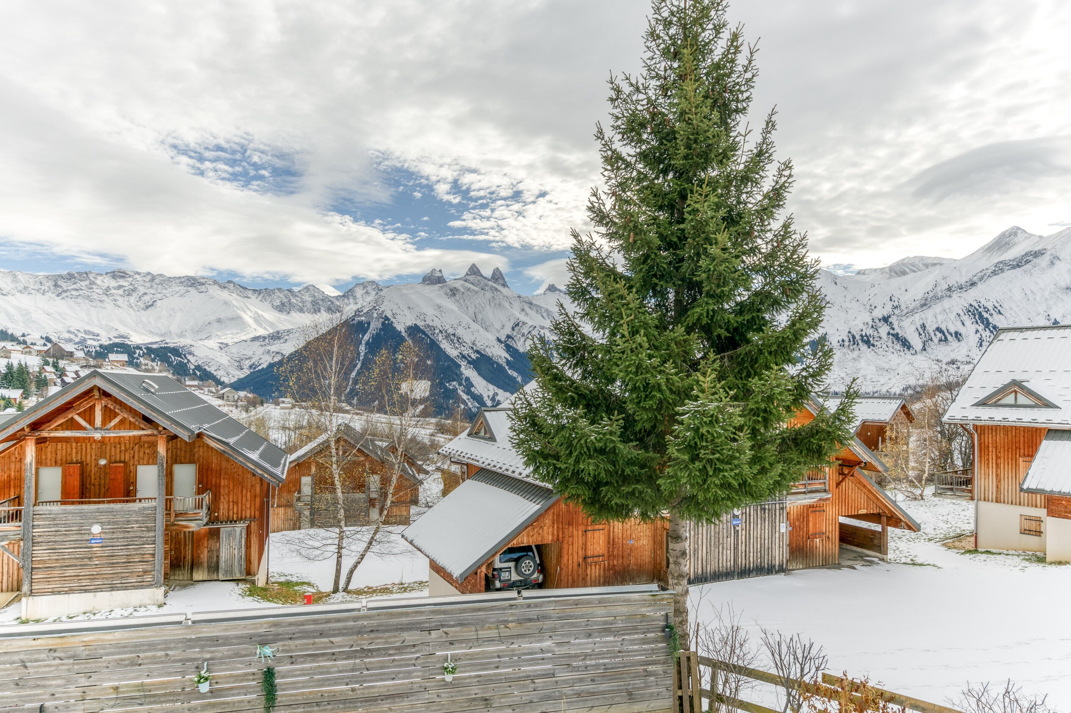 A wooden cabin with a car parked outside, surrounded by snow-covered mountains and a clear sky.