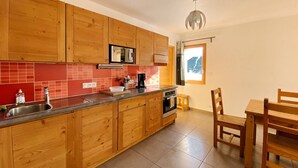 Une cuisine avec des meubles de rangement en bois, un plan de travail rouge, un évier, une cuisinière et un coin repas avec une table et des chaises.