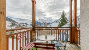 Un balcon en bois avec une table et des chaises, donnant sur un paysage montagneux enneigé.