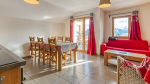 Un coin repas avec une table et des chaises, un canapé rouge et une vue sur les montagnes par la fenêtre.