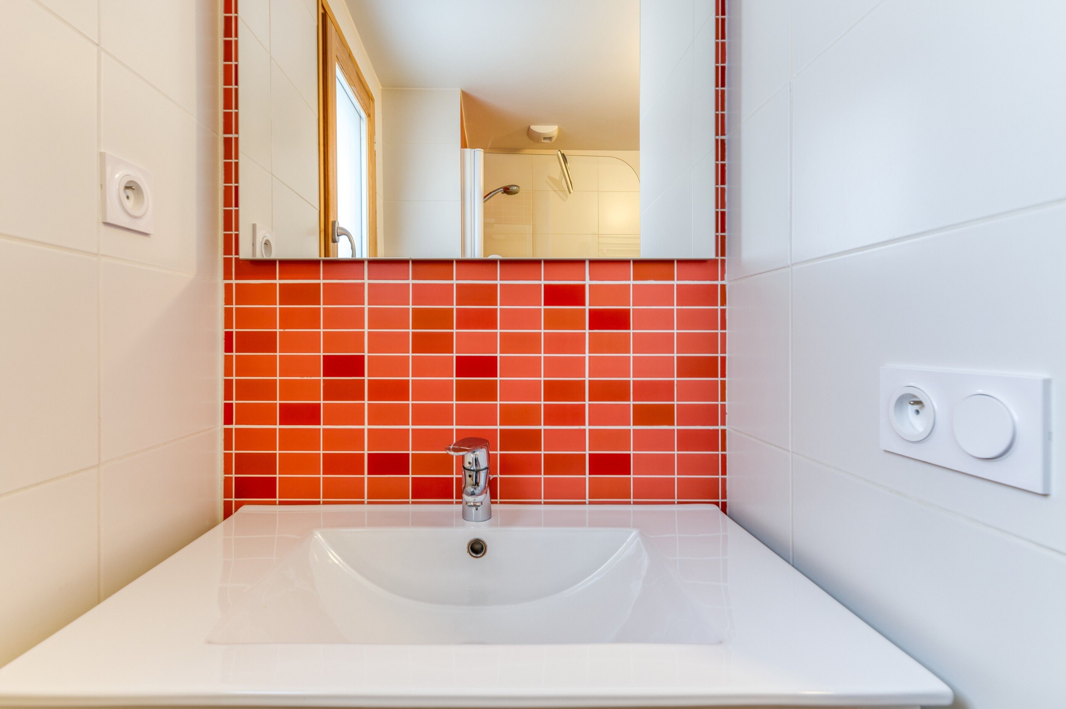 A bathroom with a white sink, a mirror, and red-tiled walls.