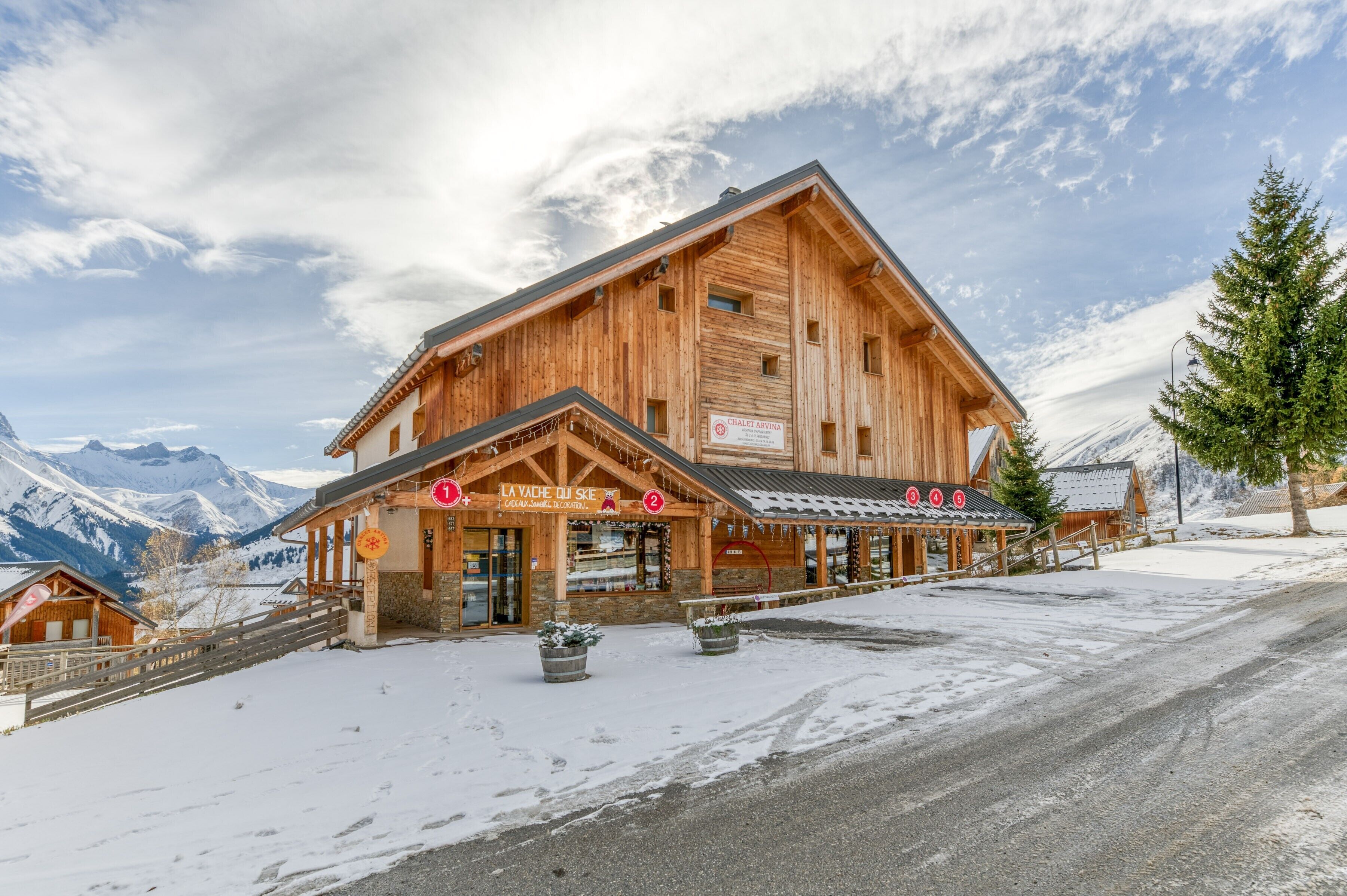 A wooden chalet with a ski slope view, a sign for 'La Vache du Ski,' and a mountain backdrop.