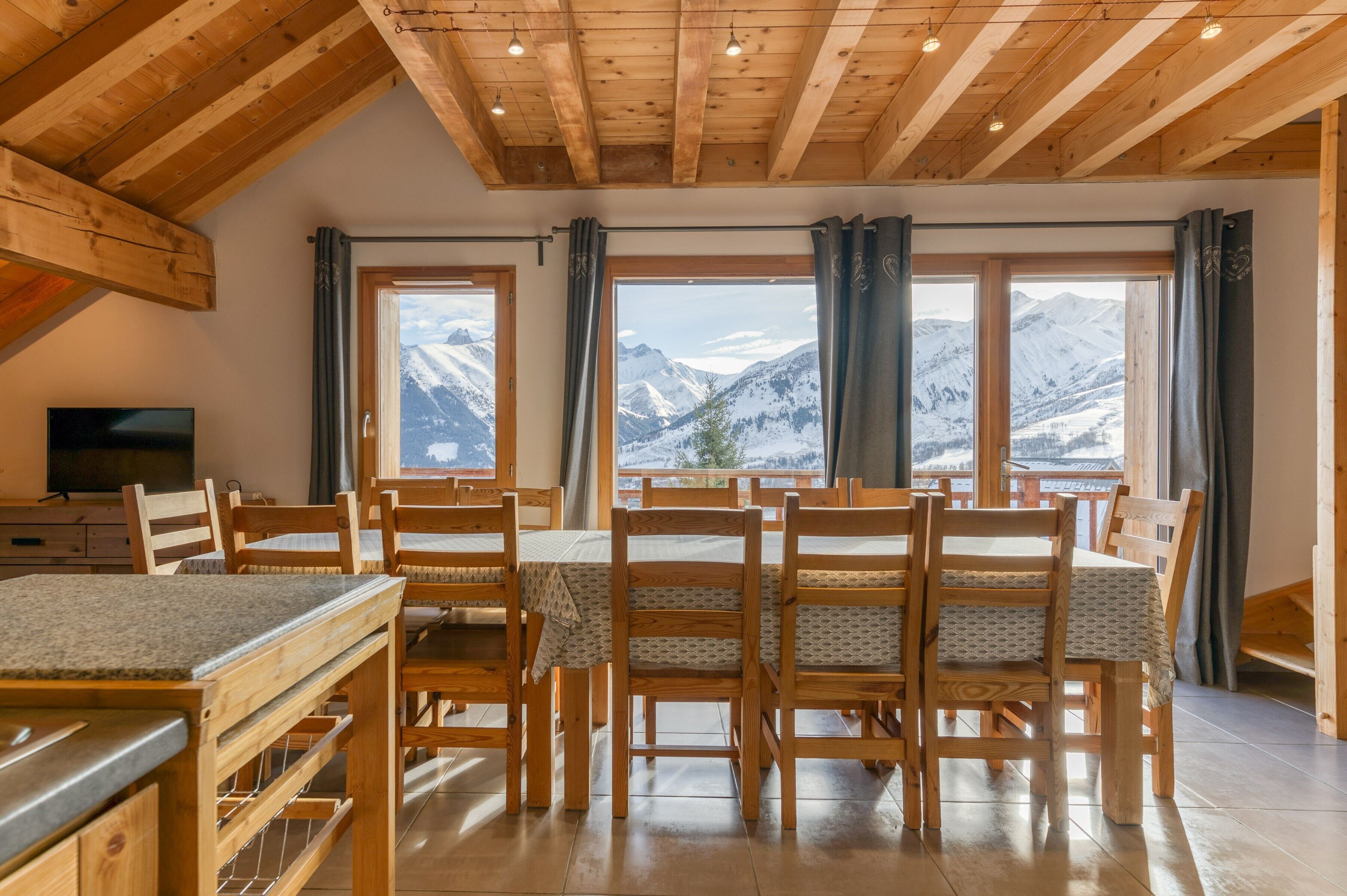Een eetgedeelte met houten meubels en uitzicht op besneeuwde bergen door grote ramen.