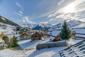 Un village enneigé, avec des chalets en bois, une clôture en bois et une chaîne de montagnes en arrière-plan.