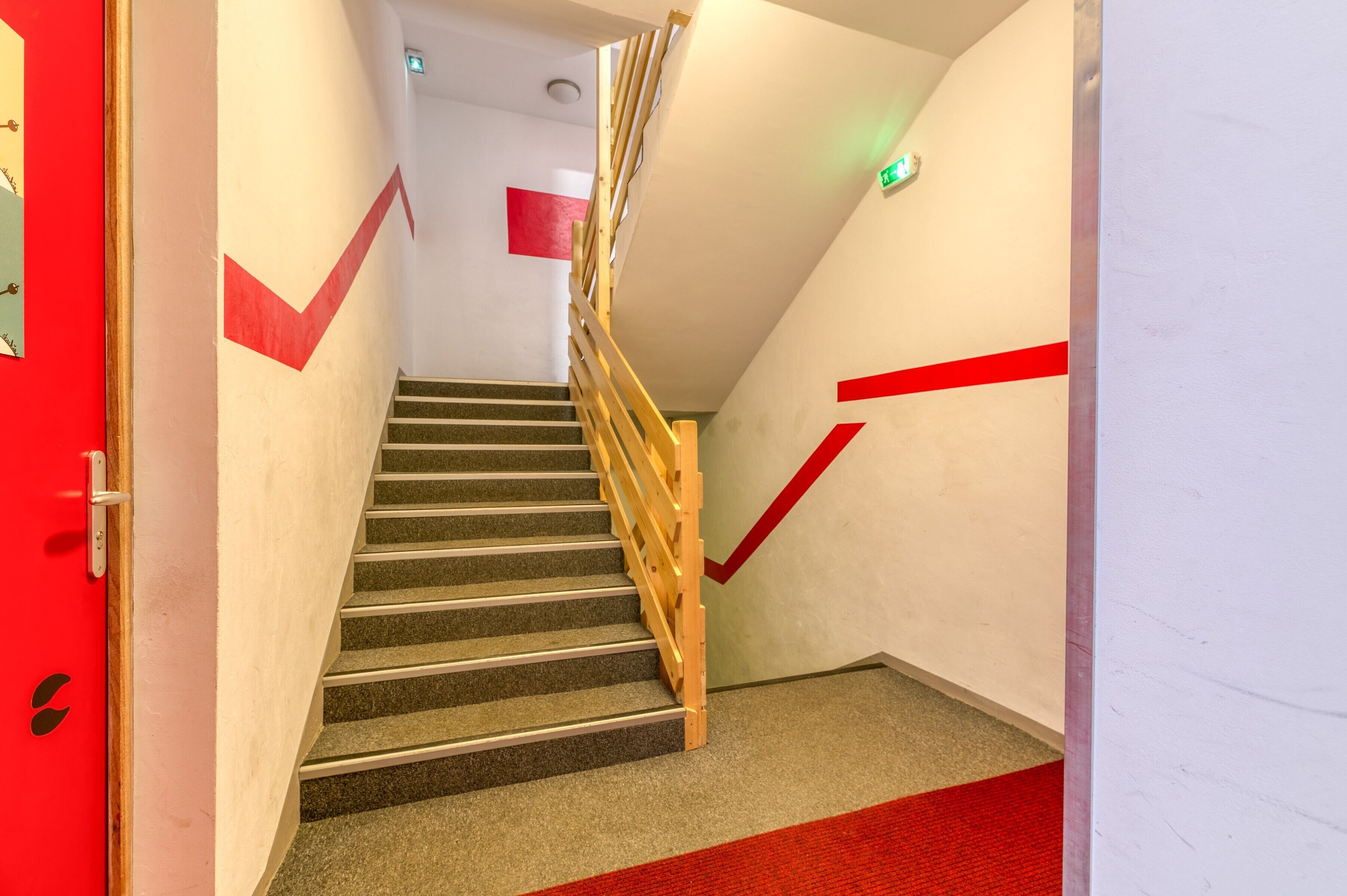 Un escalier avec un mur d’accent rouge, une main courante en bois et un tapis rouge recouvrant l’ensemble des marches.