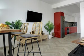 A modern kitchen with a red refrigerator, a dining area with wicker chairs, and a flat-screen TV mounted on the wall.