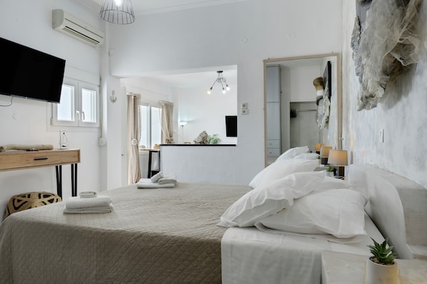 A hotel room with a bed, a desk, a TV, and a bathroom visible through an open door.