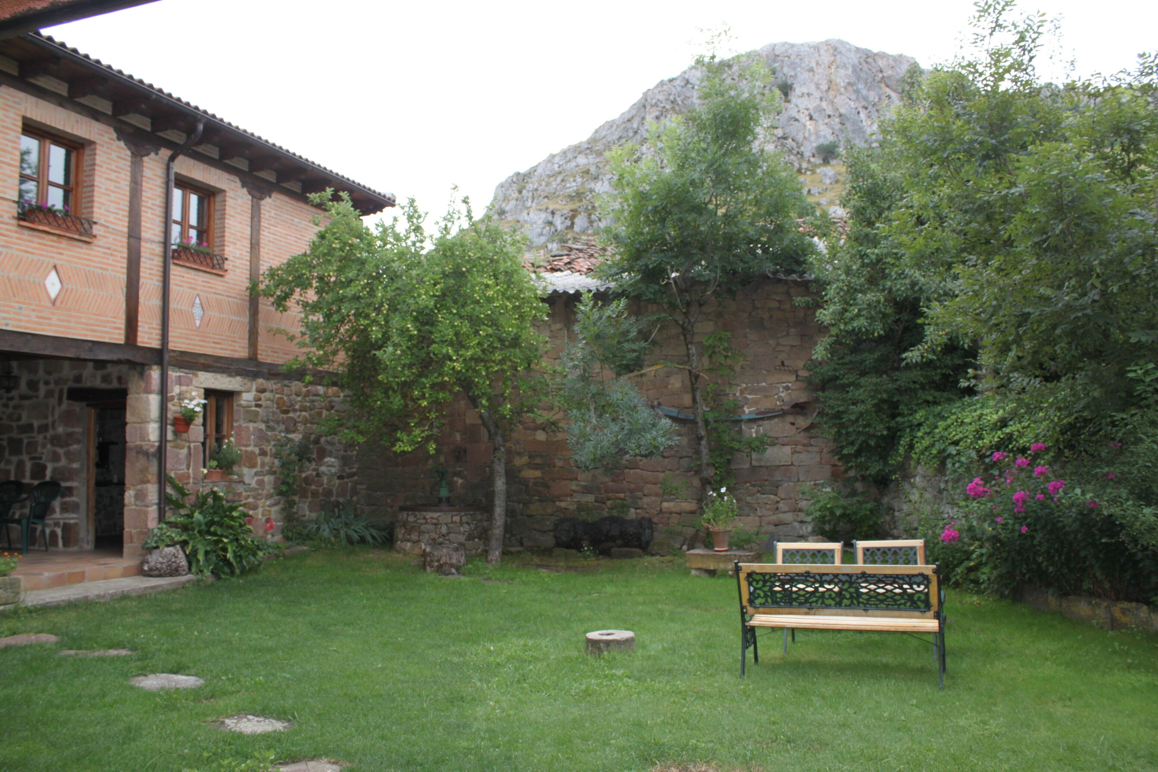 Un bâtiment en pierre avec un jardin, un banc et une montagne en arrière-plan.