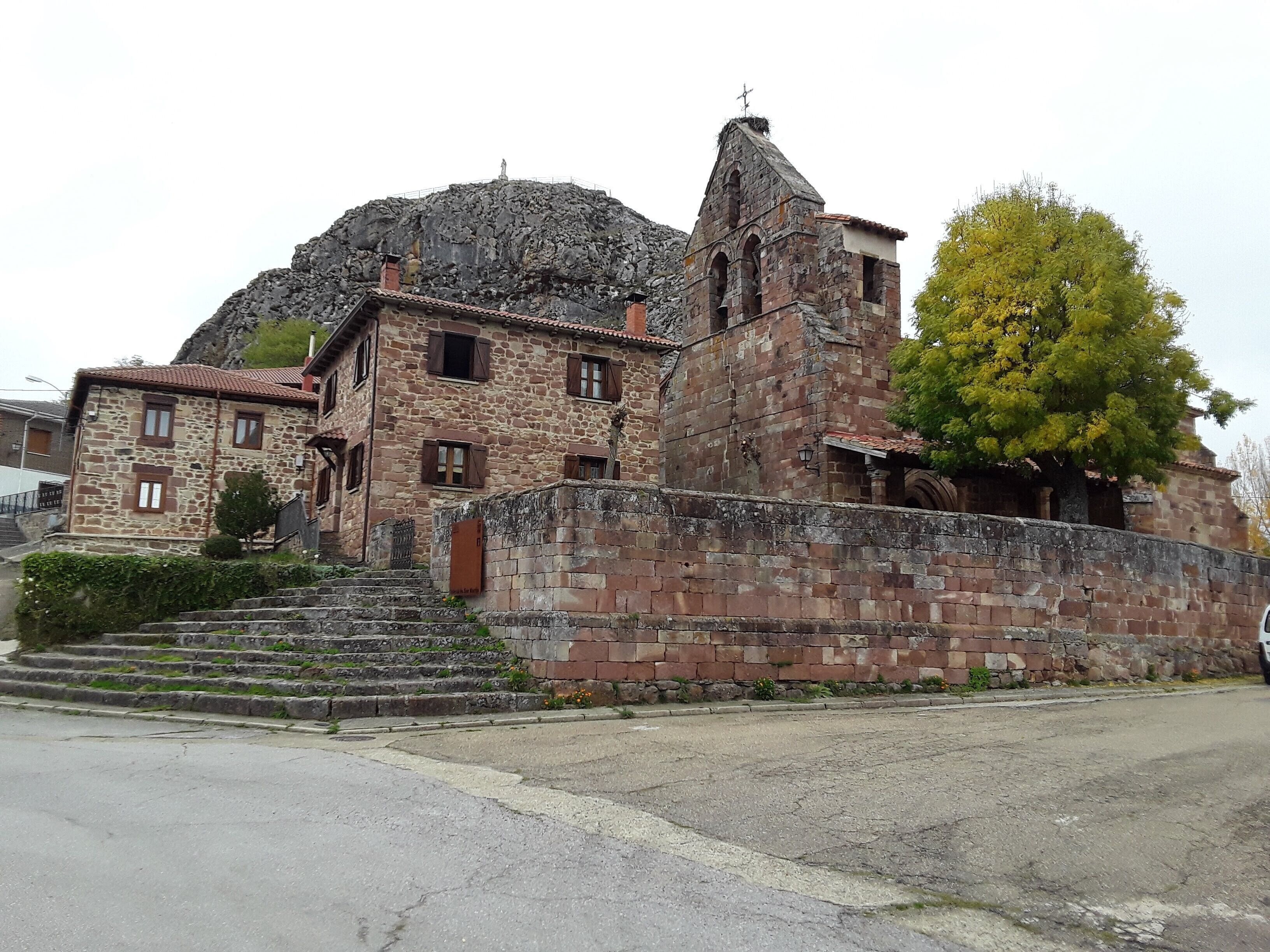 Un edificio de piedra con un campanario, una escalera que lleva a la entrada y un árbol en primer plano.