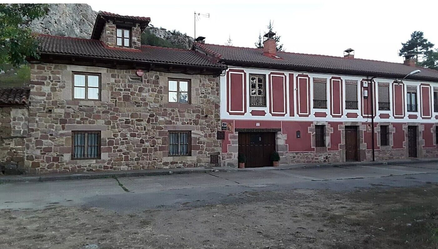A two-story stone building with a red and white facade, multiple windows, and a flat roof.