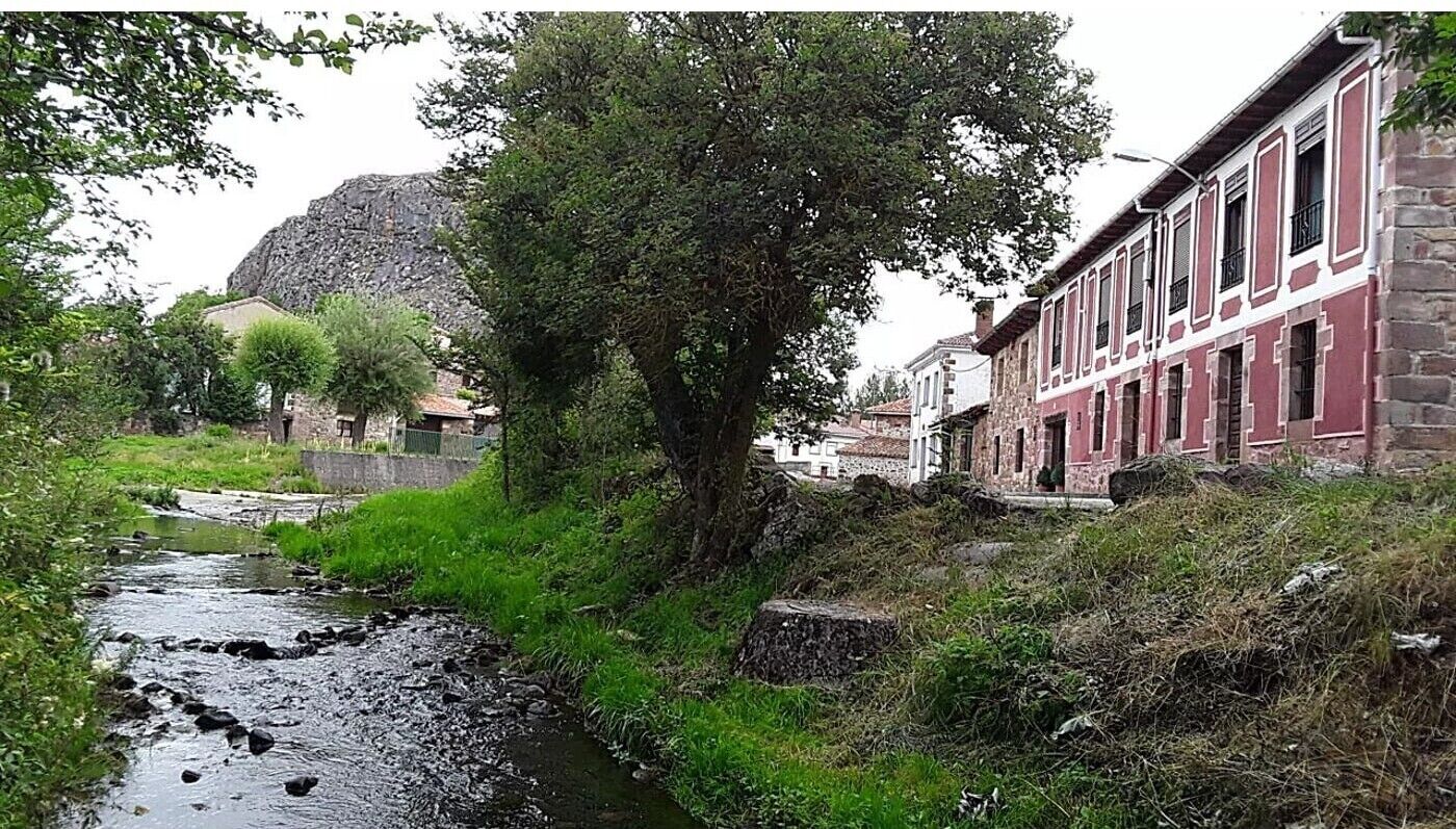 Une rivière traverse une ville où se dressent des bâtiments en pierre, et une grande formation rocheuse se profile à l’arrière-plan.