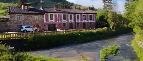 Ein Steinhaus mit roter und weißer Fassade, einem Holzzaun und einem Fluss im Vordergrund.