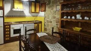 A kitchen with a stone wall, yellow cabinets, a wooden table, and a shelf with glassware.