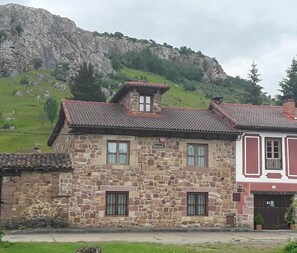 Un bâtiment en pierre avec un toit recouvert de tuiles rouges, un petit balcon et une vue sur les montagnes en arrière-plan.