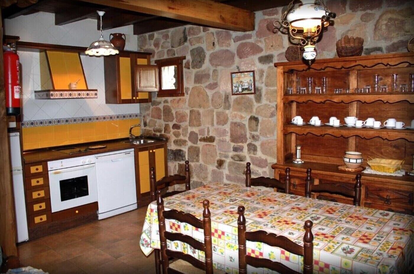 Una cocina rústica con pared de piedra, armarios de madera, un horno blanco y una mesa de comedor con sillas.