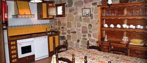 Una cocina rústica con pared de piedra, armarios de madera, un horno blanco y una mesa de comedor con sillas.