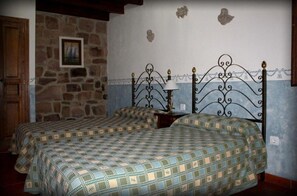 Une chambre avec deux lits, un mur en pierre et une tête de lit en métal.