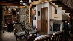 A rustic interior with a stone wall, wooden furniture, a fireplace, and a staircase.