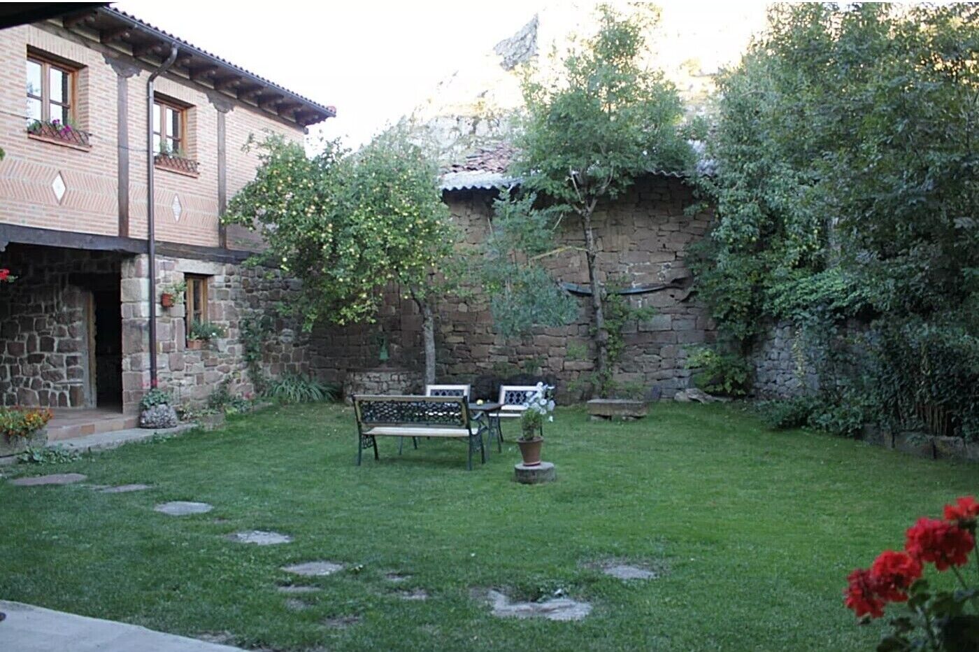 Ein Steingebäude mit Garten, einer Bank und einem Tisch.