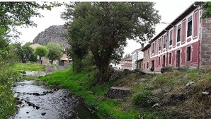 Een rivier die door een stad stroomt, met stenen gebouwen en een grote rotsformatie op de achtergrond.