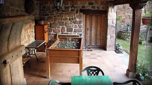Een tafelvoetbaltafel, een houten tafel en stoelen in een kamer met stenen muren en een betegelde vloer.