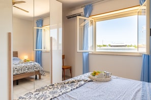 A bedroom with a bed, a chair, a window with curtains, and a mirror reflecting the room. - Apartment 'Villetta Cara Mia, Costa Merlata' with Private Terrace, Garden and Air Conditioning (Costa Merlata)