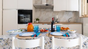 Eine moderne Küche mit weißen Schränken, einer Marmor-Spritzschutzwand, einem Einbauofen und einem Esstisch, der mit Tellern, Gläsern und einer Flasche gedeckt ist.
