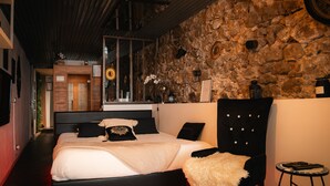 A bedroom with a stone wall, a bed with black and white bedding, a black chair, and a small table with a lamp. - Apartment 'Sweet Loft Grenoble' with Wi-Fi and Air Conditioning (Grenoble)