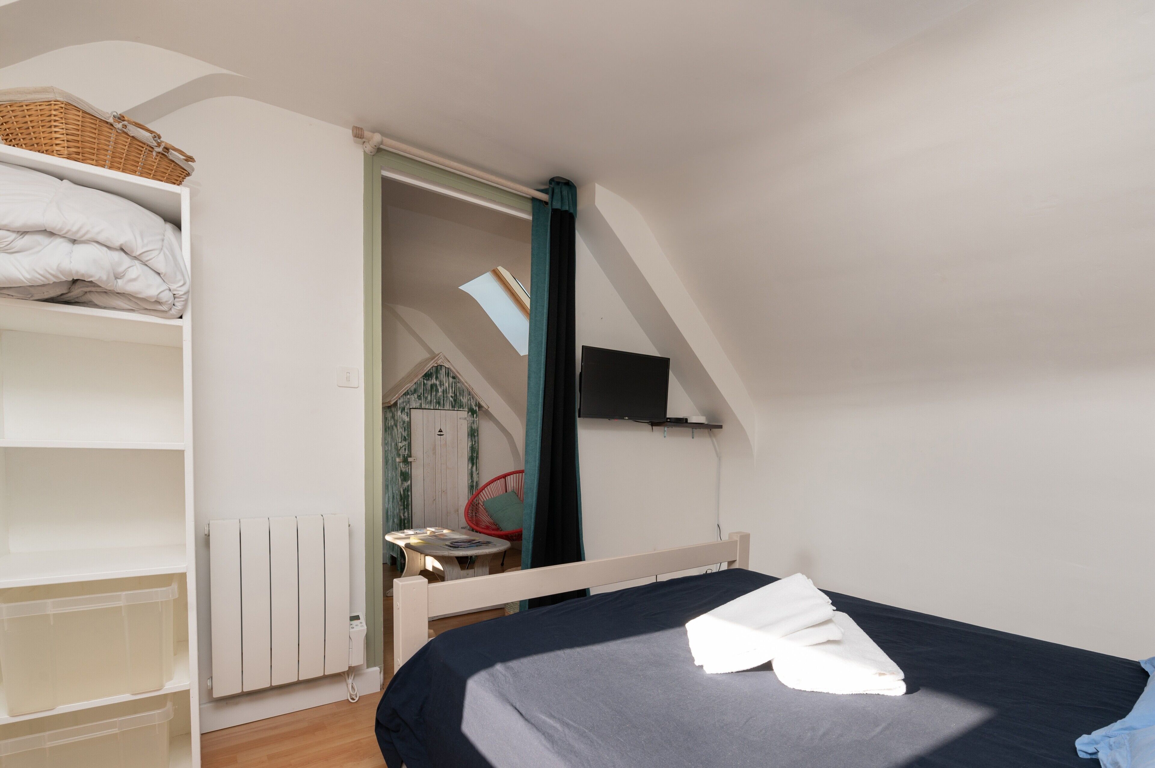 A bedroom with a bed, a wardrobe, a radiator, a television, and a skylight.