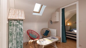 Une pièce de taille modeste, dotée d’un puits de lumière, d’une petite table sur laquelle sont posés quelques objets, de deux chaises, d’un lit et d’une armoire.