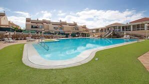 En swimmingpool med græsplæne, liggestole og en bygning med et tagtækket tag.