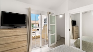 Et soveværelse med fjernsyn, en skydedør til en balkon, seng og kommode.