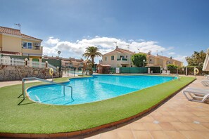 A swimming pool with a white fence, a palm tree, and houses in the background.