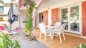 A patio with a white table and chairs, a covered seating area, and a view of a building with red shutters. - Apartment 'T2 Meublé Aux Aloès' with Mountain View, Shared Pool and Private Terrace (Cerbère)