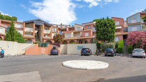 A residential building with multiple balconies, a central courtyard, and parked cars. - Apartment 'T2 Meublé Aux Aloès' with Mountain View, Shared Pool and Private Terrace (Cerbère)